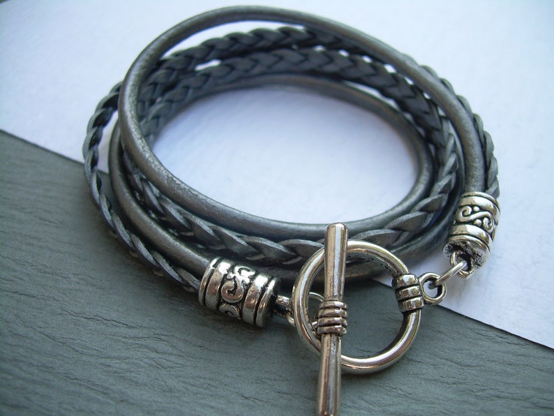 May include: A gray braided leather bracelet with a silver toggle clasp and decorative silver beads.