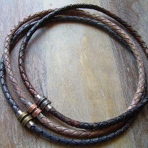 May include: Three braided leather necklaces in black, brown, and tan with silver, copper, and brass accents. The necklaces are layered on top of each other.