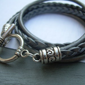 May include: A gray leather braided bracelet with a silver toggle clasp and a silver decorative accent.