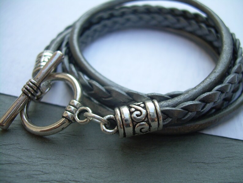 May include: A gray leather braided bracelet with a silver toggle clasp and a silver decorative accent.
