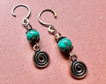 May include: Handmade earrings with turquoise beads and spiral charms. The earrings have gold-coloured hooks and accents, with a small bead cluster above the turquoise stone. The spiral charm is a bronze colour.