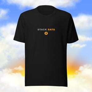 Puede incluir: Camiseta negra con el texto "STACK SATS" en gris y dorado, con un símbolo de Bitcoin dorado. La camiseta está hecha de un material suave y es adecuada para ropa casual.