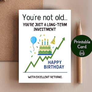 May include: A white birthday card with the text "You're not old... You're just a long-term investment." The card features a cake, balloon, and an upward trending green line graph. The words "Happy Birthday" are also on the card.