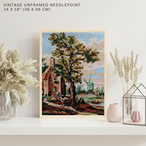 Peut inclure: Tapisserie vintage non encadrée, 36 x 56 cm, représentant une scène pastorale avec une maison, un arbre et un moulin à vent. L'œuvre a un cadre beige et un paysage coloré et détaillé.