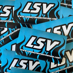 Puede incluir: Varias pegatinas azules y negras con el texto "LSV" y el sitio web "www.laurastappersvintage.com" en letras blancas. Las pegatinas tienen un diseño de llama.