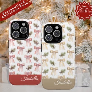 May include: Two personalized Christmas phone cases with festive designs. One case has a red base and the other a tan base. Both cases feature a pattern of bows and pine sprigs. The name "Isabella" is written on the bottom of each case.