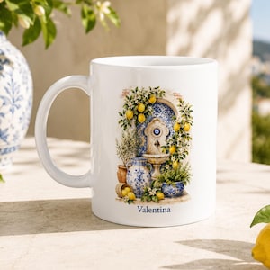 May include: A white ceramic mug featuring a colorful illustration of a stone fountain surrounded by lemon branches, blue and white pottery, and an evil eye symbol. The name Valentina is printed in blue text at the bottom of the graphic design.