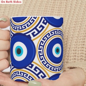 May include: White ceramic mug featuring a repeating pattern of blue and gold evil eye designs. The mug has a white handle and the text "Printed On Both Sides" is visible at the top. The mug is held by a person.