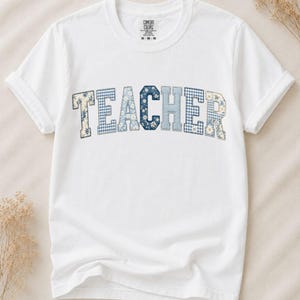 Könnte beinhalten: Ein weißes Kurzarm-T-Shirt mit dem Wort TEACHER in einer großen, gebogenen College-Schriftart. Jeder Buchstabe zeigt ein anderes Muster, darunter blau-weißes Vichy-Karo, kleine weiße Gänseblümchen und einfarbige hellblaue Texturen.