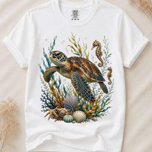 Könnte beinhalten: Ein weißes kurzärmeliges T-Shirt mit einem detaillierten Grafikdruck einer Meeresschildkröte, die zwischen Seetang, Korallen, Muscheln und zwei Seepferdchen schwimmt. Das Comfort Colors Markenetikett ist im inneren Nackenbereich sichtbar.