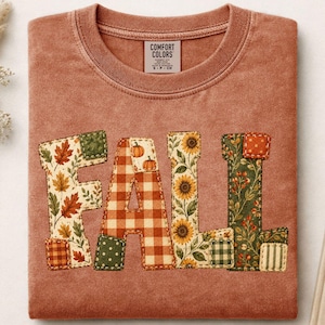 Könnte beinhalten: Ein terrakottafarbenes T-Shirt mit Rundhalsausschnitt und einem Comfort Colors-Etikett am Nacken. Auf der Vorderseite steht das Wort FALL in großen Buchstaben, die jeweils mit verschiedenen herbstlichen Mustern wie Blättern, orangefarbenem Vichy-Karo, Kürbissen, Sonnenblumen und Beeren gefüllt sind.
