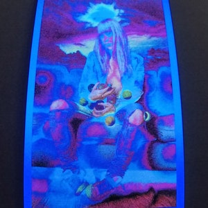 May include: A woman with long blonde hair sits on a couch, holding a handful of colorful orbs. The background is a vibrant purple and blue, with a hazy sky and mountains in the distance.