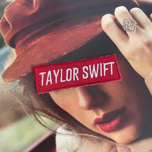 May include: A red fabric patch with white text that reads "TAYLOR SWIFT".