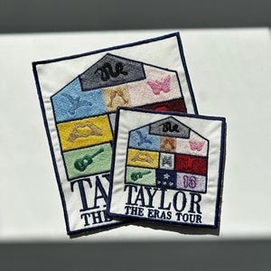 Könnte beinhalten: Zwei weiße Stoffpatches mit gestickten Bildern eines Hauses mit verschiedenen farbigen Quadraten und Symbolen. Der größere Patch sagt "Taylor The Eras Tour" und der kleinere Patch sagt "Taylor".