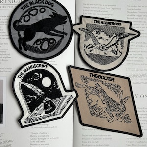 Pode incluir: Quatro patches bordados para passar a ferro com desenhos em preto e branco. Os patches representam um cão preto, um pássaro, uma pena e tinta, e uma figura a correr. Cada patch tem um título e um texto abaixo do desenho.