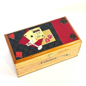 Blackjack themed wood cigar box. Top of box has a black harlequin print background with red accents. The center features a playing card motif, a martini glass, and red dice.