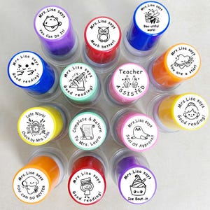 May include: A selection of self-inking stamps in various colours, each with a different cartoon image and text. Phrases include "Good reading!", "You can do it!", and "Bee-utiful work!" on the stamp faces.
