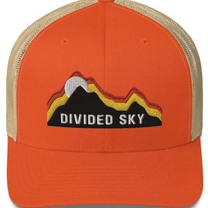 Puede incluir: Gorra de camionero naranja y tostada con un gráfico de cordillera de montañas negro, amarillo y rojo y el texto "DIVIDED SKY".