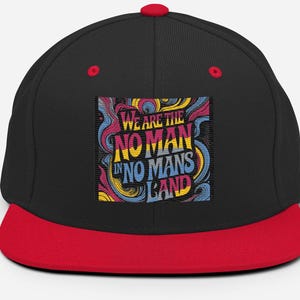 May include: Black and red snapback hat with the text "WE ARE THE NO MAN IN NO MANS LAND" in a colorful, swirling design. The hat has a red brim and top button, with red eyelets on the sides.