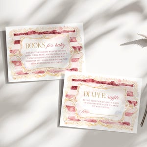 May include: Two baby shower invitation cards. One reads "BOOKS for baby" and the other "DIAPER raffle". Both cards have a watercolor design with pink and gold accents. The text is in a delicate, elegant font.