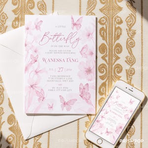 An elegant flat lay image featuring a soft pink baby shower invitation card surrounded by beautiful pink and white floral arrangements and paper butterfly decorations. The card includes delicate watercolor butterfly illustrations and sophisticated pink script typography that reads "A Little Butterfly is On the Way," inviting guests to a baby shower honoring Wanessa Tang. Soft shadows and natural light add depth to the image, creating a romantic, refined.
