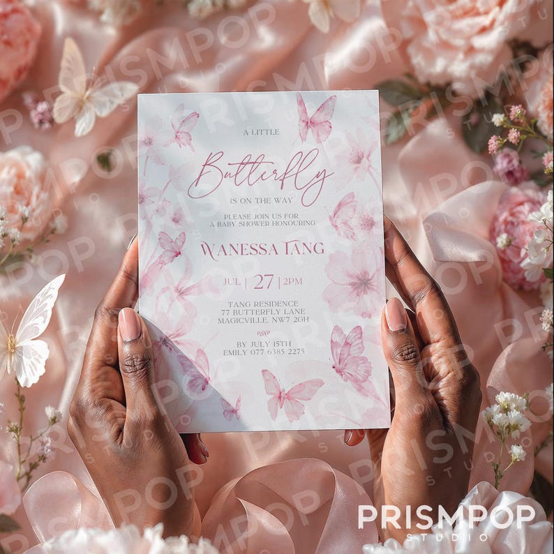 An elegant, soft-toned image showing a close-up of a delicate pink floral baby shower invitation card held gently by two hands. The invitation features watercolor-style pastel pink butterflies and flowers along with graceful script typography reading "A Little Butterfly is on the Way," honoring Wanessa Tang. Surrounding the invitation are luxurious elements including silky pink fabric, delicate white butterfly decorations, soft pink and white flowers, and lush greenery, creating a romantic.