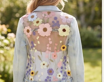 May include: A light blue denim jacket featuring a sheer back panel adorned with colorful floral embroidery. The design includes various flowers in shades of pink, yellow, purple, and blue, with long sleeves, a collar, and a buttoned hemline.