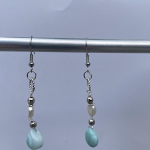 May include: A pair of silver dangle earrings with a light blue teardrop-shaped stone, a white pearl, and silver beads.