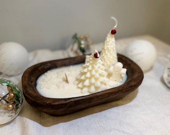 May include: A white candle shaped like two Christmas trees in a wooden bowl. The candle is surrounded by white wax flakes.