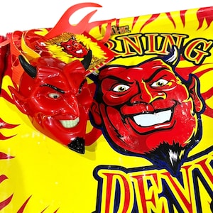 May include: A red devil mask with black horns and a smiling face is displayed next to a yellow and red sign with the word "DENNYS" in blue and yellow lettering. The sign also features a devil face graphic and the word "NING".