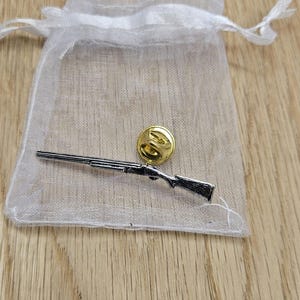 May include: A silver shotgun pin with a gold-coloured back, in a white organza bag.