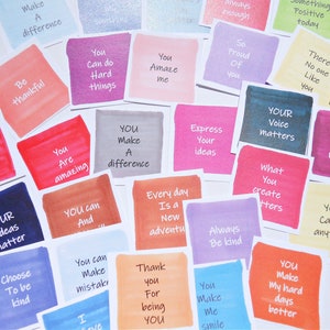 May include: A collection of square paper cards featuring watercolor-style backgrounds in various colors including pink, blue, yellow, and orange. Each card displays a unique motivational phrase in black text, such as You Can do Hard things, You Amaze me, and YOUR Voice matters.