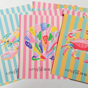 May include: A stack of colorful stationery cards with marine life illustrations. Each card features a different design: a lobster, a seashell, and a crab. The cards have striped backgrounds and the text "A Little Note for You".