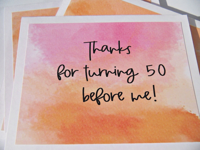 May include: A watercolor card with a pink and orange background. The card says "Thanks for turning 50 before me!"