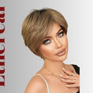 May include: A woman wearing a short, layered, light brown wig with a side-swept bang. The word "Ethereal" is written in red vertically on the left side of the image. She is wearing a gold necklace with a heart pendant.