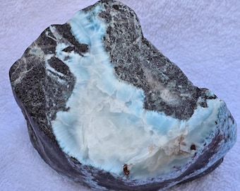 May include: A large, irregularly shaped piece of blue and white cabochon with a dark grey matrix. The cabochon has a smooth, polished surface and a natural, rough edge.