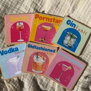 Puede incluir: Juego de seis posavasos cuadrados de madera con ilustraciones de cócteles. Cada posavasos muestra un cóctel diferente: Spritz, Pornstar Martini, Gin Tonic, Vodka Martini, Old Fashioned Cocktail y Cosmopolitan Cocktail. Los posavasos tienen un diseño retro con fondos coloridos.