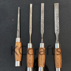 Pode incluir: Quatro formões para entalhar madeira com detalhes em metal prateado. Os cabos são feitos de madeira castanha clara com um padrão de grão único. As lâminas dos formões têm um design padronizado. Os formões estão dispostos em fila sobre uma superfície escura.