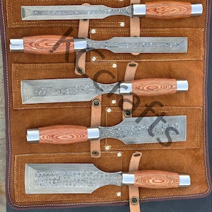 Könnte beinhalten: Satz von sechs Meißeln mit Holzgriffen in einer braunen Lederrolle. Die Meißel haben eine gehämmerte Oberfläche und sind in einer Reihe angeordnet.