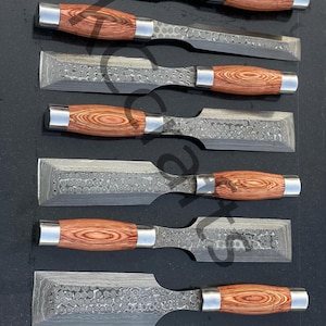 May include: A set of seven chisels with patterned steel blades and wooden handles. The handles are a warm brown color with a wood grain pattern, and are capped with silver metal ferrules. The blades have a textured, hammered appearance.