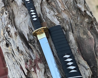 Puede incluir: Una katana negra y blanca con una vaina negra. La katana tiene un patrón de diamante blanco en el mango y la vaina.