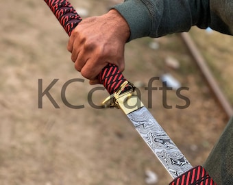 Puede incluir: Una espada decorativa con una hoja estampada y un mango rojo y negro. El mango está envuelto en un patrón entrecruzado. La espada tiene una guarda dorada. El texto "KCrafts" es visible.