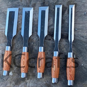 Puede incluir: Cinco cinceles para carpintería con hojas de acero brillante y mangos de madera con un patrón de vetas de madera marrón claro. Los cinceles están dispuestos en fila, mostrando sus bordes afilados y su artesanía.