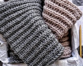 Può includere: Due sciarpe di lana, una grigia e una rosa chiaro, sono piegate e poste all'interno di una scatola foderata con carta velina bianca.