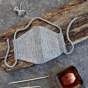 May include: A gray knitted face mask with a simple design. The mask has two long ties that can be tied behind the head.