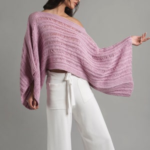 A young girl is wearing a light pink knit summer boatneck sweater with wide sleeves. The sweater features stockinette, garter stitch and three types of drop stitches.