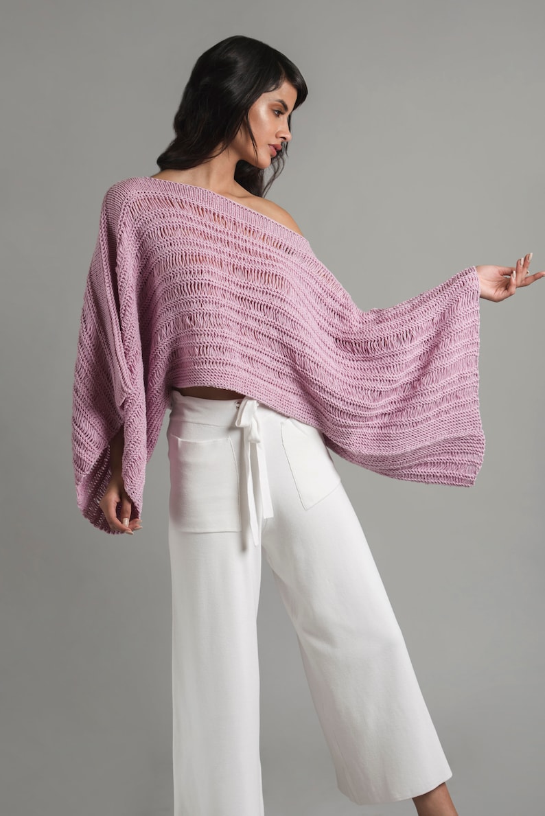A young girl is wearing a light pink knit summer boatneck sweater with wide sleeves. The sweater features stockinette, garter stitch and three types of drop stitches.