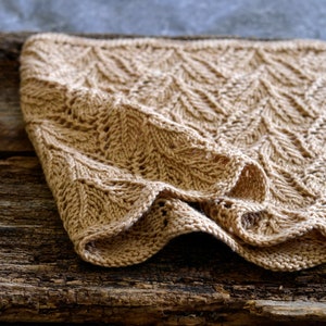 Könnte beinhalten: Eine beige gestrickte Decke mit Chevron-Muster, gefaltet und auf einer rustikalen Holzoberfläche platziert.