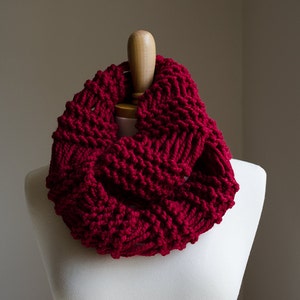 Puede incluir: Una bufanda infinita de punto de color rojo oscuro con un patrón texturizado. La bufanda se muestra en un maniquí blanco.