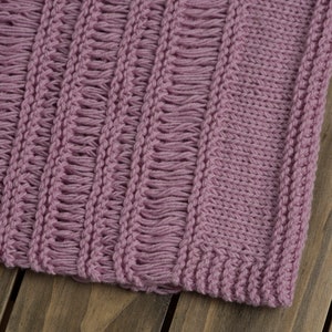 Close-up of a light pink hand knit summer sweater top with stockinette, garter stitch and three kinds of drop stitches.